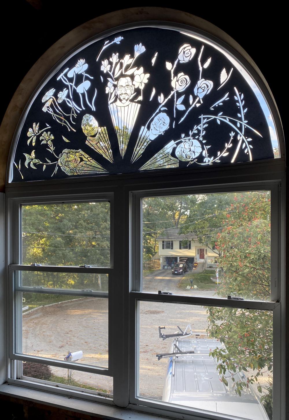 Single sheet of black paper cut into a 5’ semicircle and placed in a window of matching size.  The semicircle is divided into five sections with a person’s portrait and flowers cut out in each. 