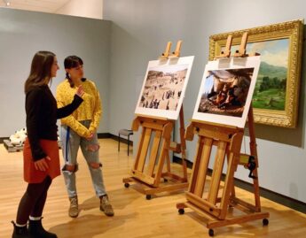 Engagement Intern Charlotte Smith ’24 looking at two photographs by Lynsey Addario.