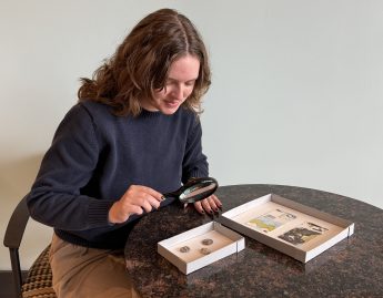 a young woman examines coins with a magnifying glass