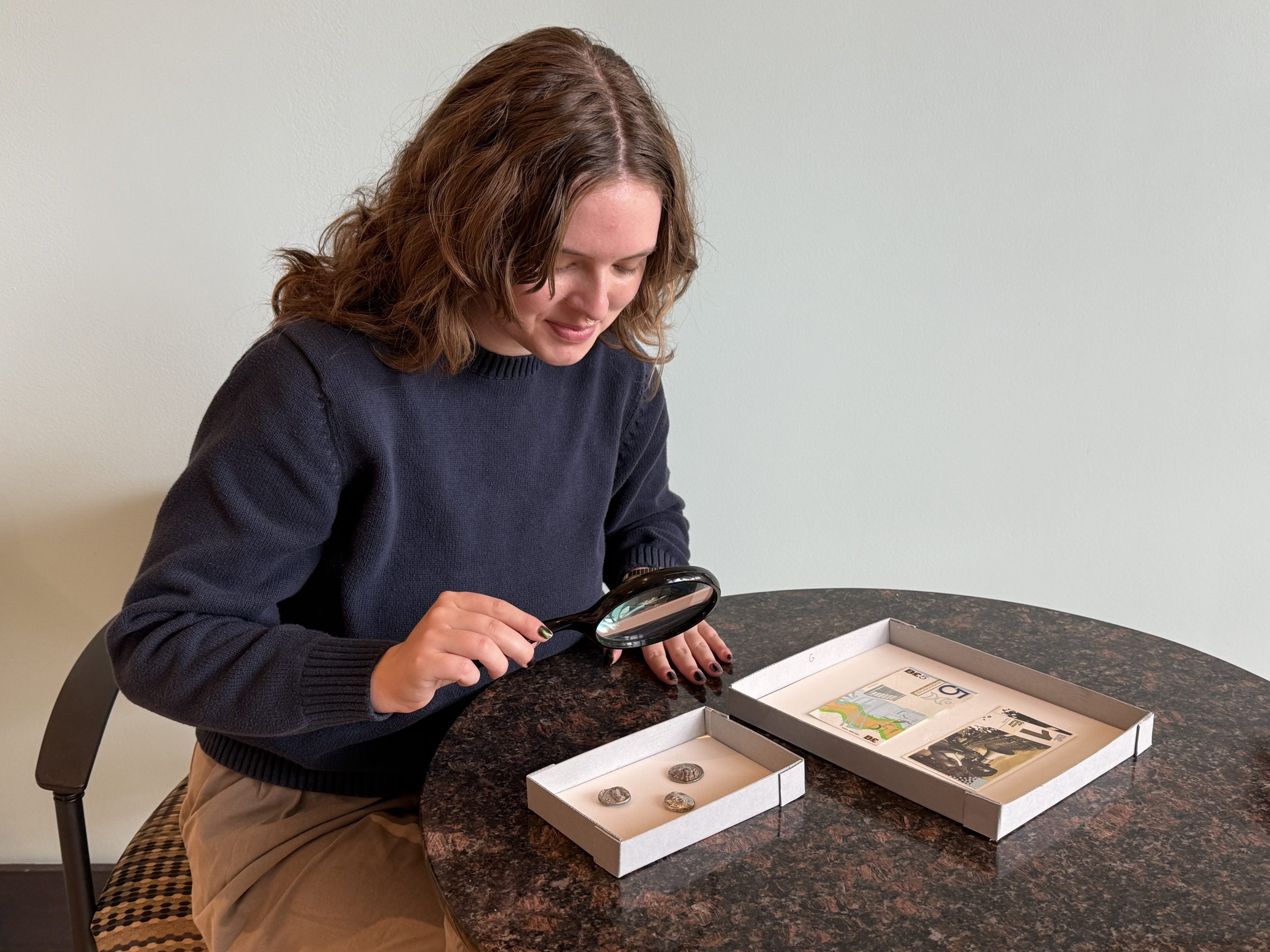 a young woman examines coins with a magnifying glass