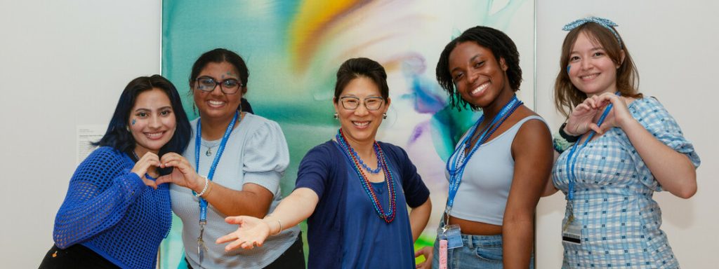 Four students with Tricia Paik in the center, all wearing blue, in front of a colorful artwork